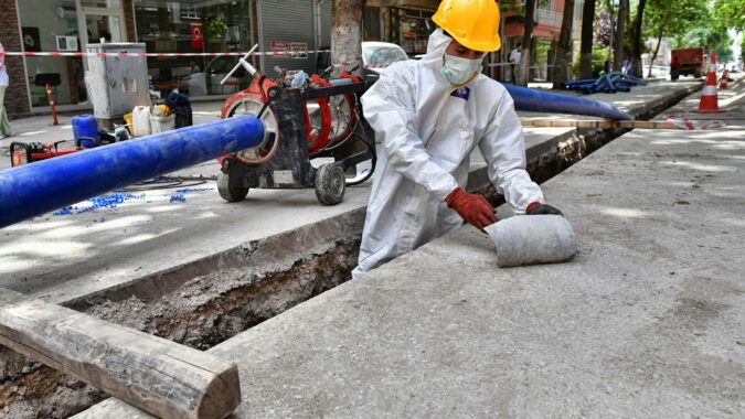 man wearing PPE removing asbestos from a pipe in the street.