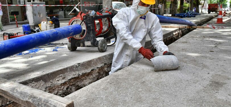 man wearing PPE removing asbestos from a pipe in the street.